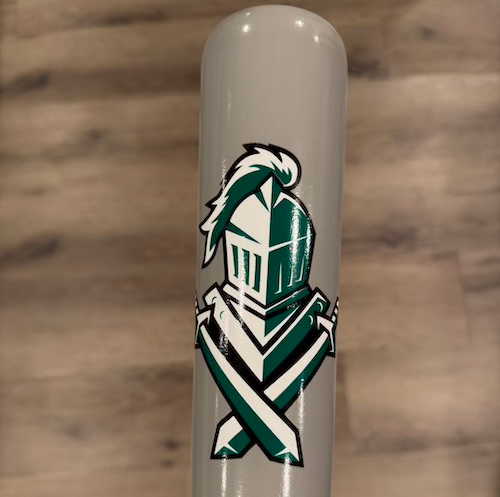 Close-up of a gray Caliburn fungo bat barrel with a custom green, white, and black knight helmet and crossed swords logo.