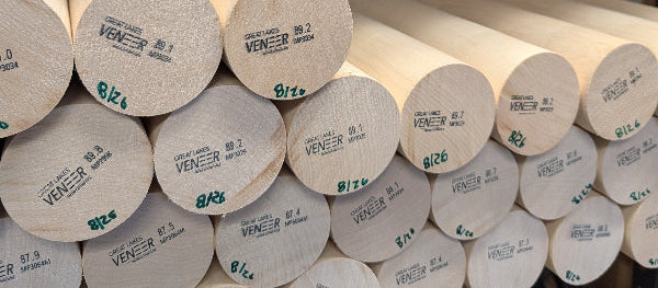 Multiple light natural wood cylindrical rods or dowels stacked on black metal shelves, with printed labels visible on the round ends.